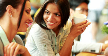 Conversazione in lingua inglese; giovane lavoratrice con colleghi durante una pausa caffè